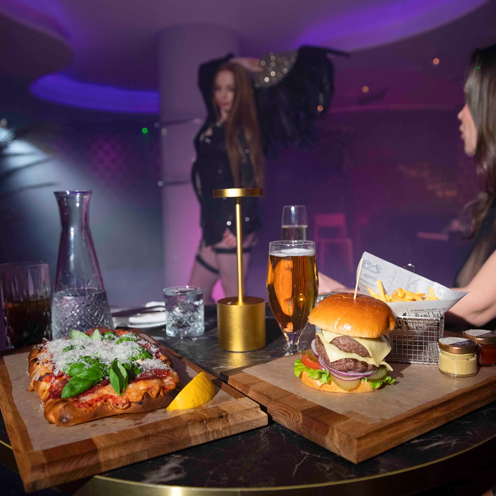 Burgare, pizza och drinkar serveras vid bord framför show på nattklubben Velvetroom i Stockholm.
