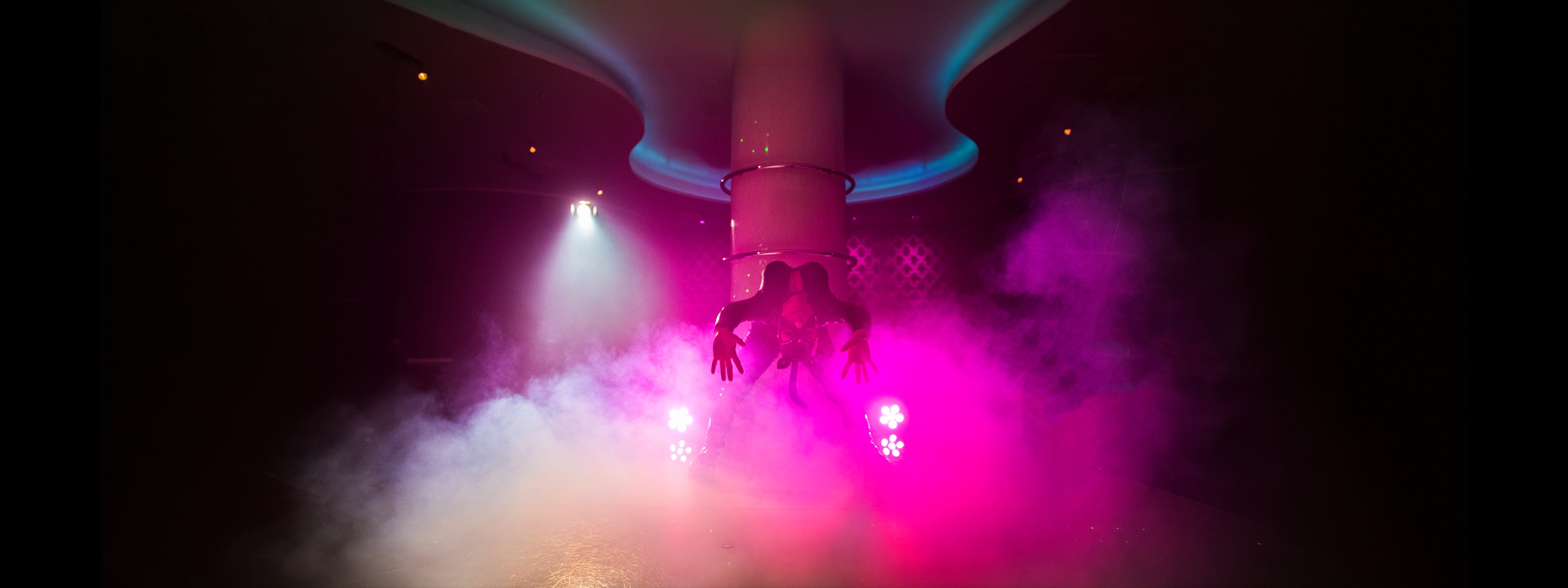 Showdansare i catsuit lutar sig bakåt framför pelare i neonbelyst klubbmiljö på Velvetroom i Stockholm.